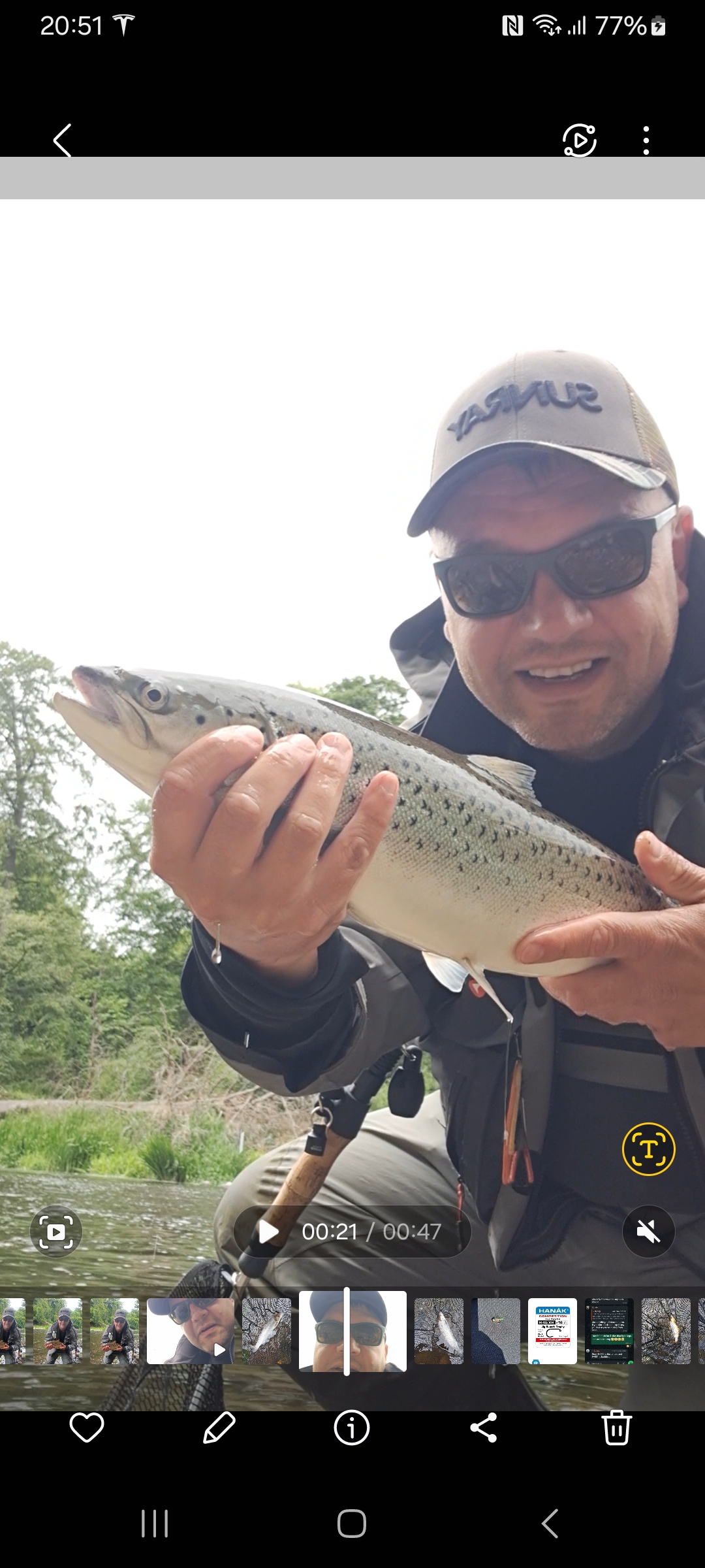 Adrian smiling and holding a fish beside the river