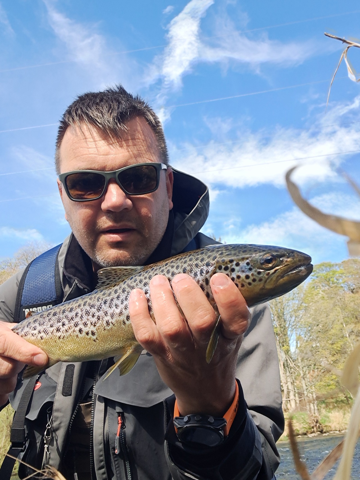 Adrian holding a brown trout beside the river
